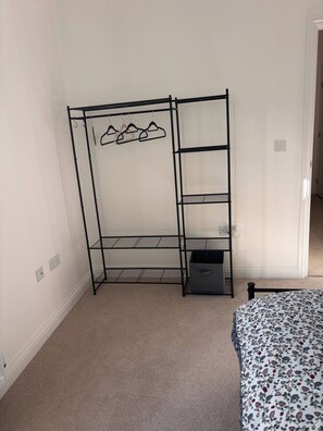 A room with a black metal wardrobe, a bed with a floral bedspread, and a carpeted floor. - Charming Ground Floor Apartment Near Beach, Norfolk (Sheringham)