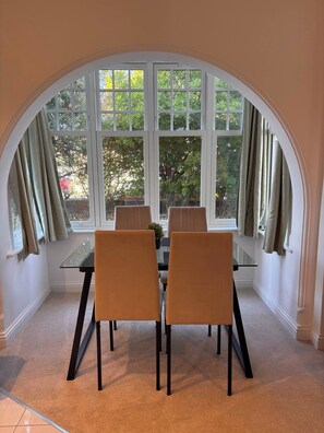 A dining area with a table and chairs, large windows, and curtains. - Charming Ground Floor Apartment Near Beach, Norfolk (Sheringham)