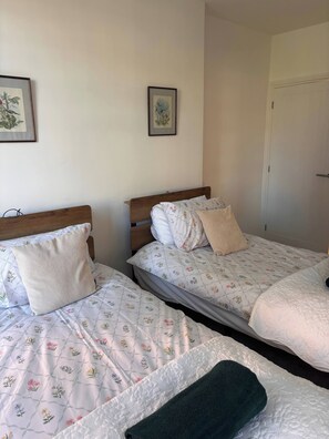 A room with two beds, each with floral-patterned bedding and wooden headboards. - Charming Ground Floor Apartment Near Beach, Norfolk (Sheringham)