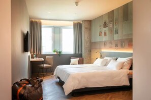 Ein Hotelzimmer mit einem Bett, einem Schreibtisch, einem Stuhl, einem Fernseher und einer Wand mit gerahmten Bildern.