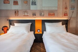 Ein Hotelzimmer mit zwei Betten, einer Wanduhr und einer Auswahl an Handtaschen darüber.