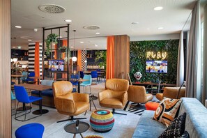 Ein moderner Lounge-Bereich mit Ledersesseln, einem farbenfrohen Hocker und einem Neon-Schild mit dem Schriftzug 'PLAY'.