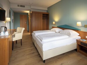 Ein Hotelzimmer mit Bett, Schreibtisch, Stuhl, Fernseher und Kleiderschrank.