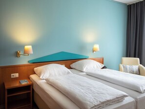 Ein Hotelzimmer mit zwei Betten, einem Schreibtisch, einem Stuhl und zwei Wandlampen.