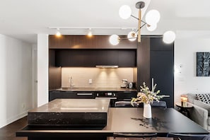 A modern kitchen with dark cabinetry, a marble island, and a pendant light fixture. - Charming 2-bedroom apartment with AC in lovely Montréal (Montréal)