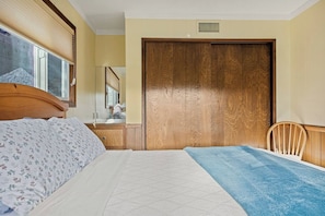 A bedroom with a bed, a wooden wardrobe, a chair, and a window with blinds. - Tree-Laden Crestline Cabin | 3BR + Fireplace (Crestline)