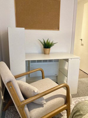 Una habitación con un escritorio blanco, una planta pequeña en maceta, una silla y un tablón de anuncios fijado a la pared.