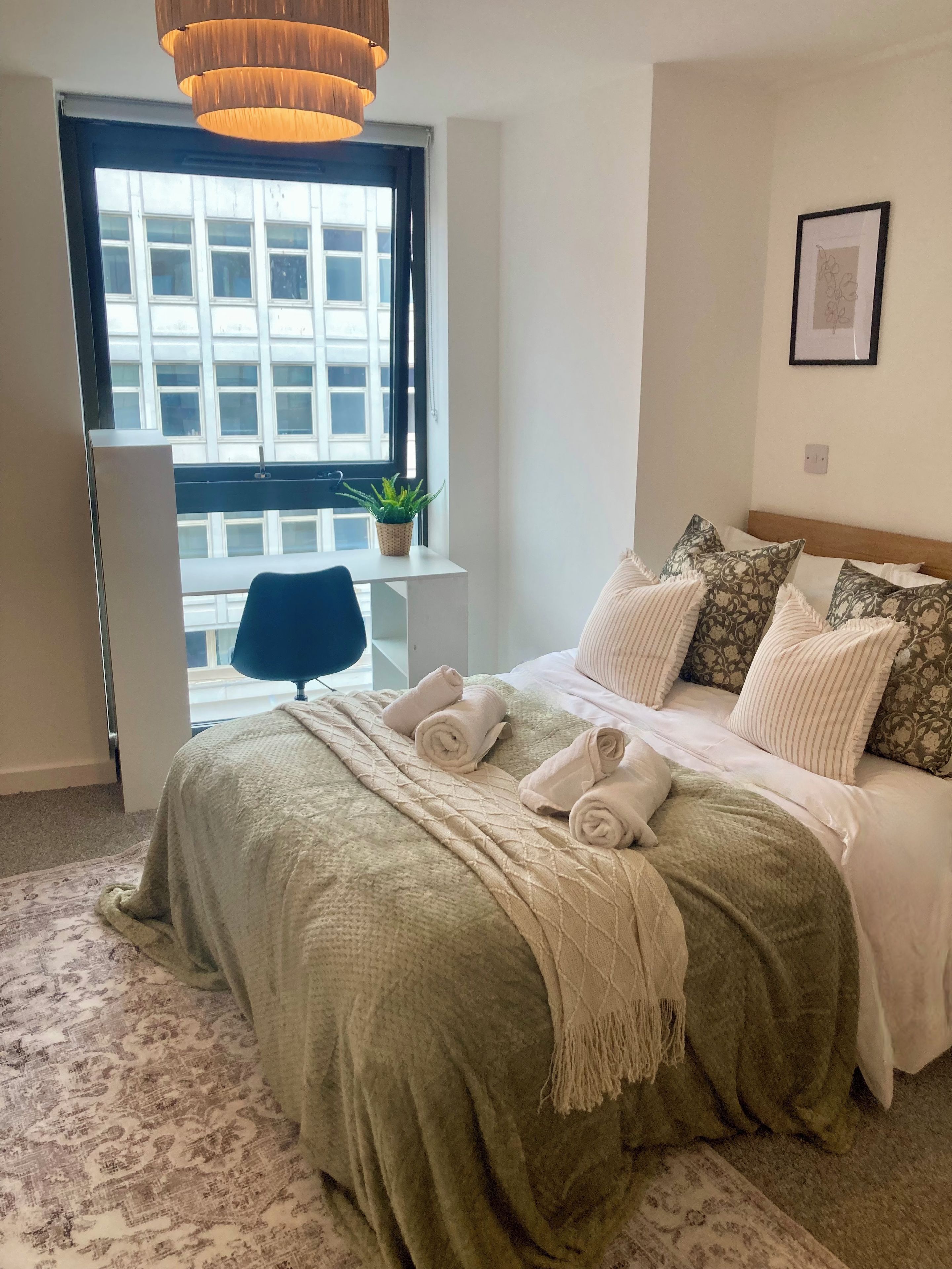 A bedroom with a bed, a window, a chair, a plant, and a hanging light fixture.