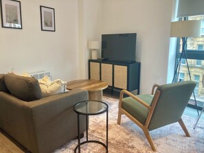 Una sala de estar moderna con un sofá, una mesa redonda de centro, una silla, un televisor y un aparador.