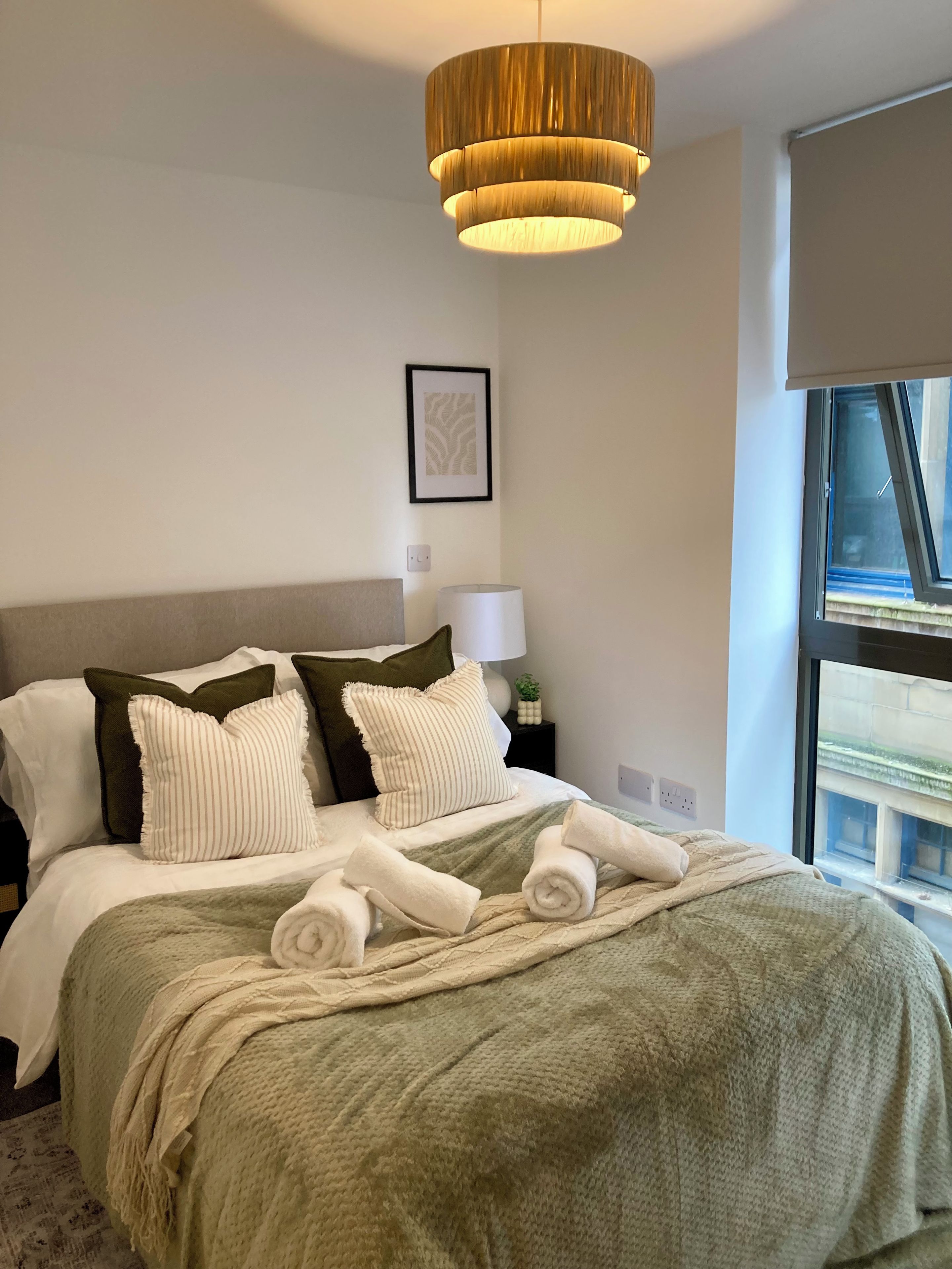 A hotel room with a bed, a bedside lamp, a window, and a hanging light fixture.