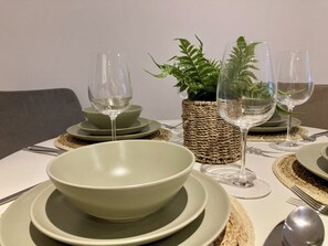 A dining table set with multiple green plates, bowls, and clear wine glasses, accompanied by a woven basket containing green foliage. - Fargate Central 204 | 3-Bed | Sheffield Centre (Sheffield)