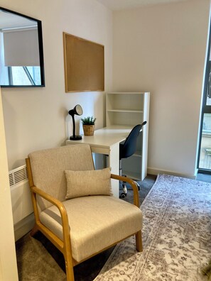 A room with a wooden chair, a desk, a lamp, a small plant, and a patterned rug. - Fargate Central 204 | 3-Bed | Sheffield Centre (Sheffield)
