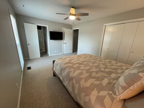 Une chambre à coucher comprenant un lit, un ventilateur de plafond, une armoire et un téléviseur.