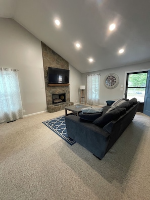 A modern living room with a stone accent wall, a flat-screen TV, a fireplace, a sofa, and a large window. - Cozy Lake House 2 (Macon)