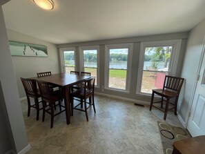 A dining area with a large table and chairs, large windows with a view of a lake and greenery, and a painting on the wall. - Cozy Lake House 2 (Macon)
