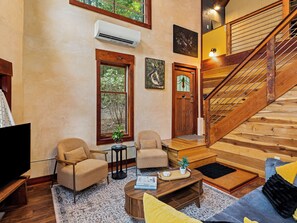 Un vaste espace de vie agrémenté d’un escalier en bois, de deux fauteuils, d’une table basse et d’un téléviseur.