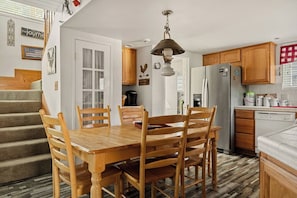 Une cuisine avec des meubles de rangement en bois, une table à manger avec des chaises, un réfrigérateur et une machine à café.