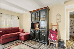 A room with a red sofa, a dark wooden cabinet with glass doors, a patterned rug, and a birdcage. - Lake Arrowhead Cabin | Sleeps 10 | Dog-Friendly (Lake Arrowhead)