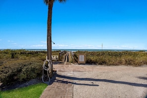 A paved pathway leading to a beach with a wooden signboard and a palm tree. - Gulf-view 2BR condo with balcony, pool, WiFi, and beach access. (Boca Grande)