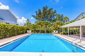 A rectangular swimming pool with a clear blue water surface, surrounded by a paved deck and a covered seating area with chairs. - Gulf-Front Bliss | Soothing Waves, Breathtaking Sunsets & the Peaceful Charm of Boca Grande (Boca Grande)