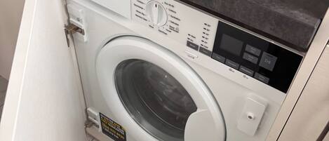 A front-loading washing machine with a control panel, a countertop above it, and a tiled floor.