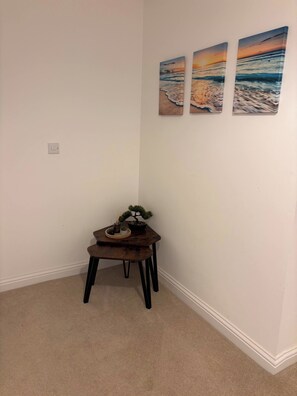 A corner room with a small table, a potted plant, and three wall-mounted paintings. - Spacious 3-bedroom Apartment Near Norfolk Beach (Sheringham)