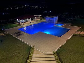 Una piscina con zona de estar techada y una pequeña estructura, rodeada de un césped cuidado y escalones que dan a la piscina.