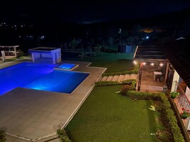 Una piscina con una pequeña estructura adyacente, un césped bien cuidado y un edificio con terraza.