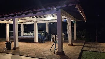 Un espacio al aire libre techado con cama, sillas y una parrilla.