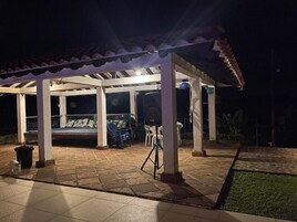 Un espacio al aire libre techado con cama, sillas y una parrilla.