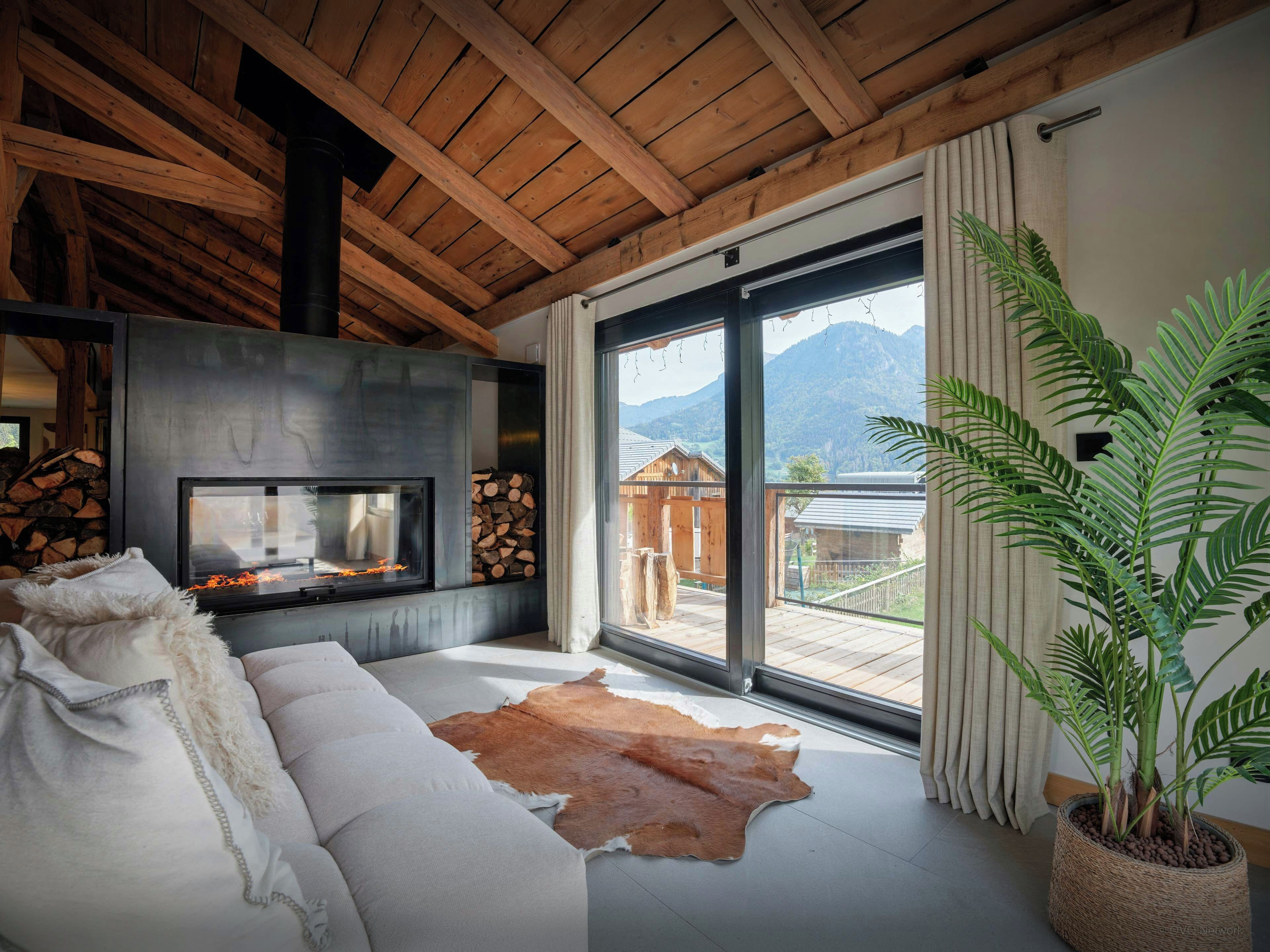 Una sala de estar moderna con chimenea, un sofá, un tapete de cuero y un ventanal con vistas a la montaña.