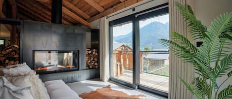 A modern living room with a fireplace, a sofa, a leather rug, and a large window with a view of a mountain.