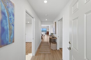 Corredor com portas brancas, chão de madeira e vista para uma sala de jantar com mesa e cadeiras.