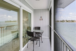A balcony with a glass door, wicker chairs, a small round table, and decorative items. - BG North 81 | Top-Floor Gulf Escape—Golden Sunsets, Endless Skies, Soothing Surf & Pickleball (Boca Grande)