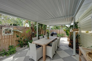 Un patio cubierto con mesa y sillas para comer, rodeado de macetas con plantas y una valla de madera.