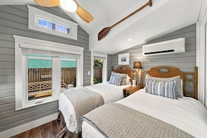 Un dormitorio con dos camas, ventilador de techo, equipo de aire acondicionado y ventana con vistas al exterior.