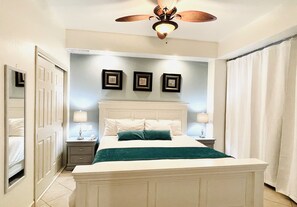 A bedroom with a bed, nightstands, a ceiling fan, and wall-mounted artwork. - Las Palomas 1 BR Oceanview, Lazy River, Heated Pools (Puerto Peñasco)