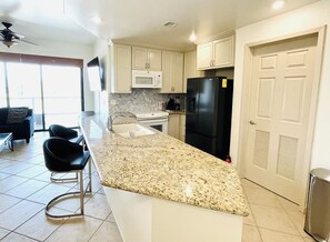 A kitchen with a granite countertop, stainless steel appliances, and a dining area with a black chair. - Las Palomas 1 BR Oceanview, Lazy River, Heated Pools (Puerto Peñasco)