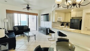 A modern living room with a sofa, coffee table, and chairs, a kitchen with appliances, and a ceiling fan. - Las Palomas 1 BR Oceanview, Lazy River, Heated Pools (Puerto Peñasco)