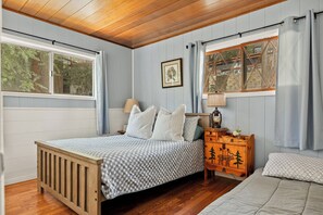 Een slaapkamer met een houten bed, een nachtkastje met een lamp, een raam met gordijnen en een aan de muur bevestigd schilderij.