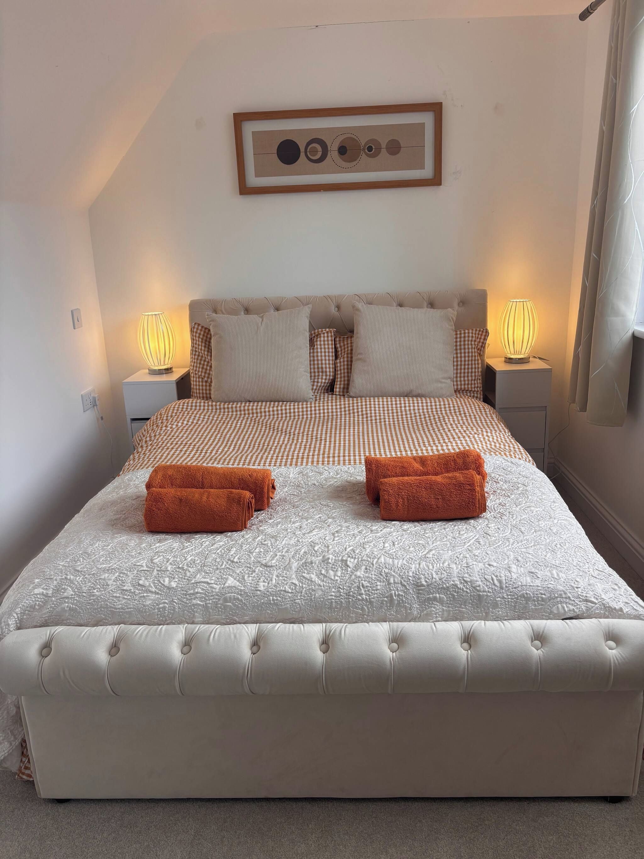 Une chambre à coucher avec un grand lit, deux lampes de chevet, un tableau encadré au mur et une fenêtre avec des rideaux.