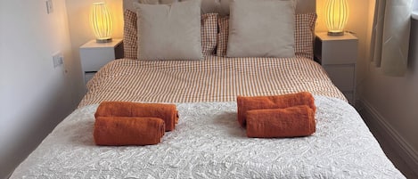 Un dormitorio con una cama grande, dos lámparas de noche, un cuadro enmarcado en la pared y una ventana con cortinas.