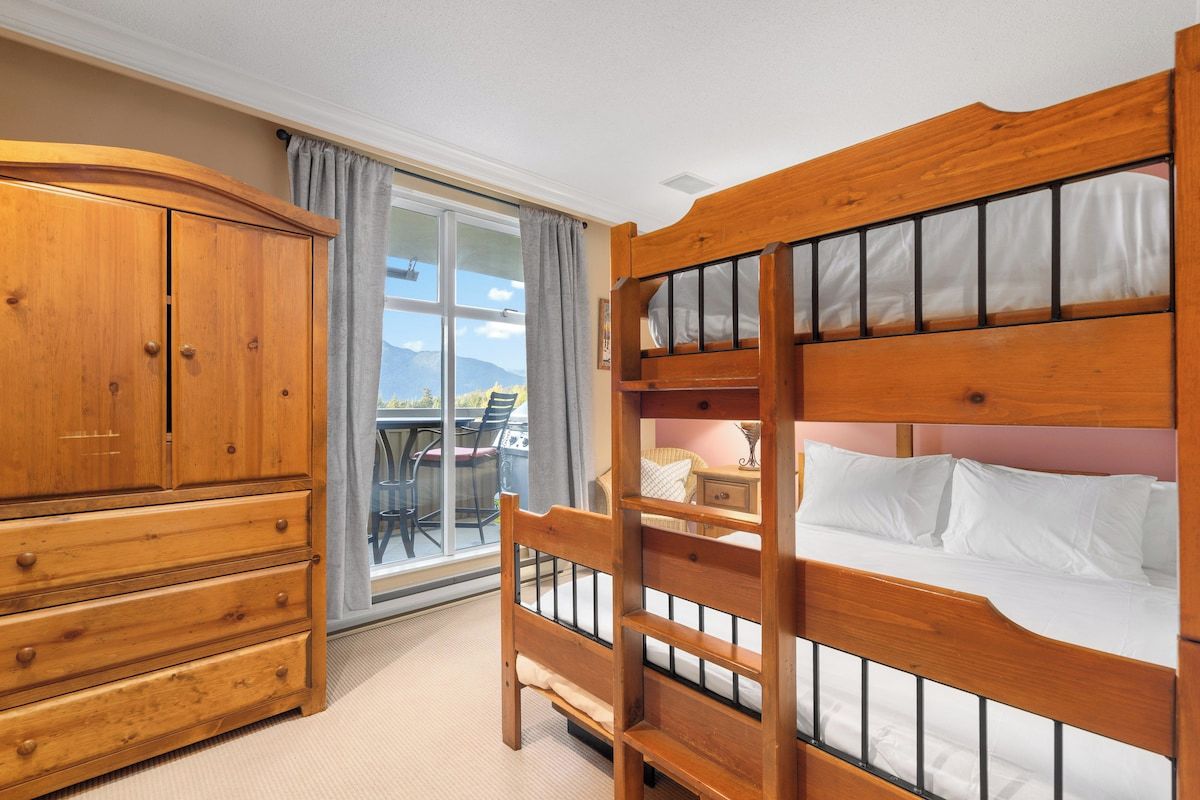 A bedroom with a bunk bed, a wooden wardrobe, and a sliding glass door leading to an outdoor area.