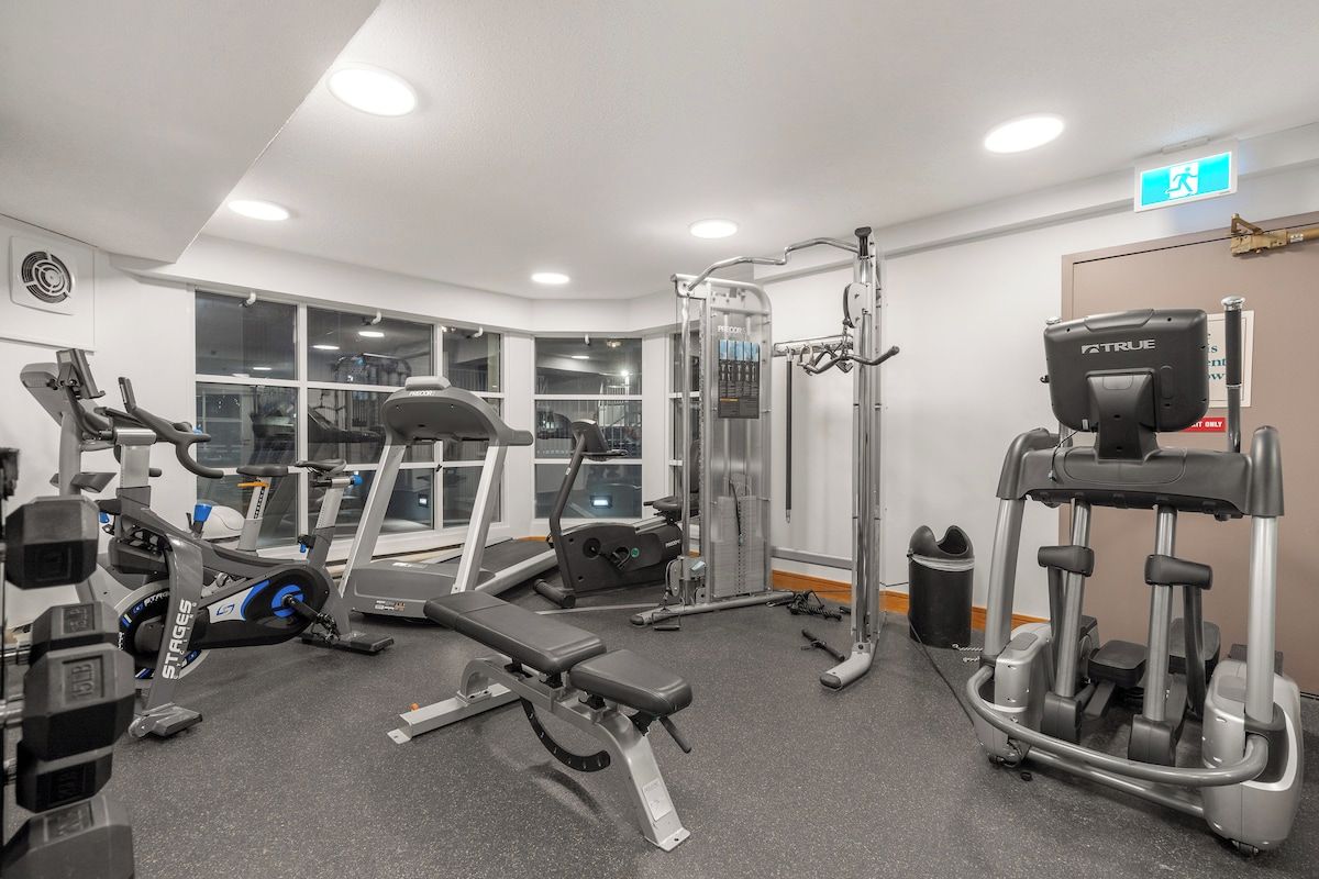 A gym with various exercise equipment, including treadmills, weight machines, and a bench.