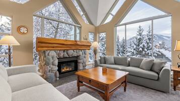 A cozy living room with a stone fireplace, large windows, and a view of snow-covered trees.