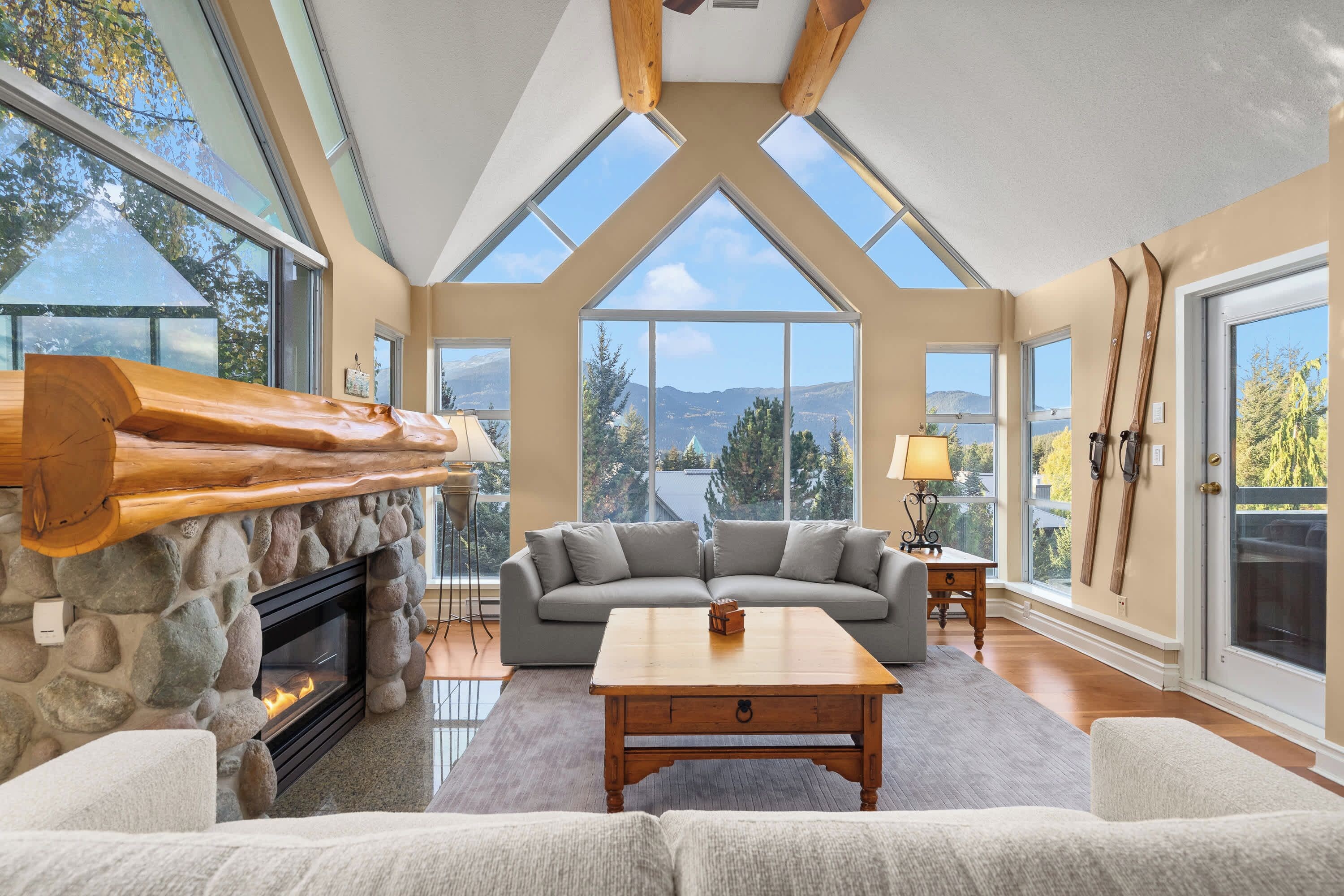 Un salon spacieux avec une cheminée en pierre, une grande fenêtre donnant sur les montagnes et un coin salon confortable.