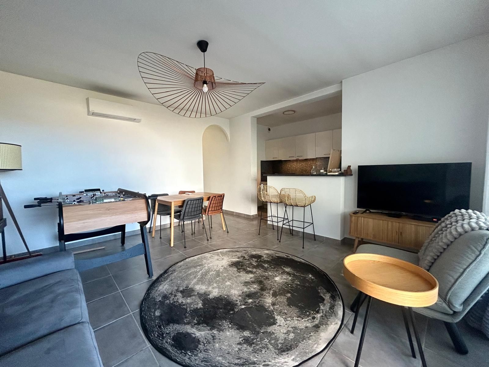 A modern living room with a round coffee table, a dining area with chairs, a kitchen area with a TV, and a sofa.