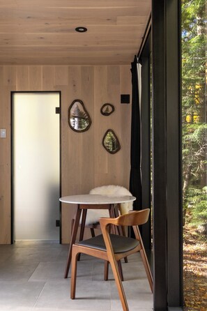 Quarto com teto de madeira, mesa redonda com uma cadeira e uma porta.