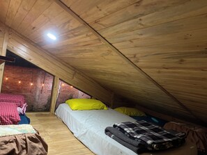 A cozy attic bedroom with a sloped ceiling, a brick wall, and a bed with pillows.