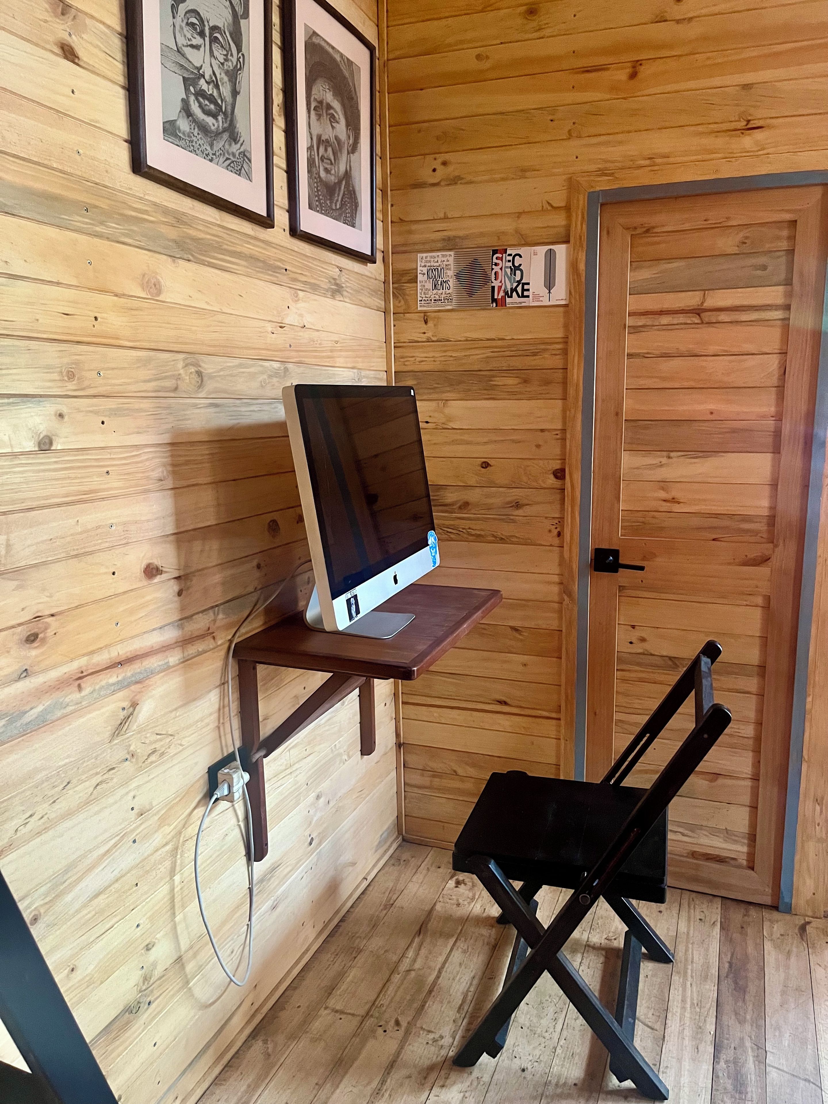 Un intérieur en bois avec un bureau sur lequel se trouve un ordinateur portable, une chaise pliante noire et deux tableaux encadrés accrochés au mur.